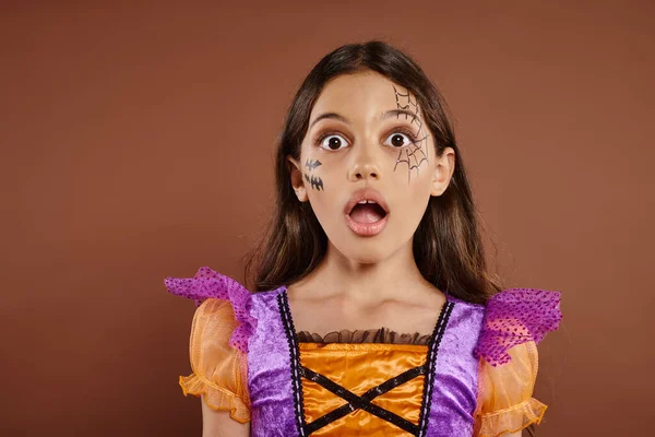 stock image face expression, shocked girl in Halloween costume looking at camera on brown backdrop, spooky