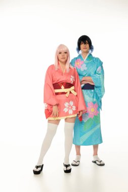 Anime tarzı geleneksel kıyafetleri ve perukları içinde beyaz kameraya uzun uzun bakan bir çift.