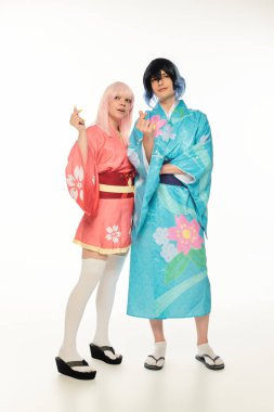 full length of young anime couple in bright kimonos showing mini hearts signs with fingers on white clipart