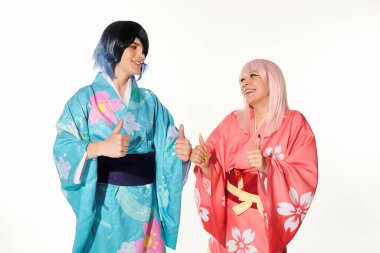 Renkli kimonoları ve perukları olan neşeli kozcular başparmaklarını kaldırıp beyazlar içinde birbirlerine bakıyorlar.