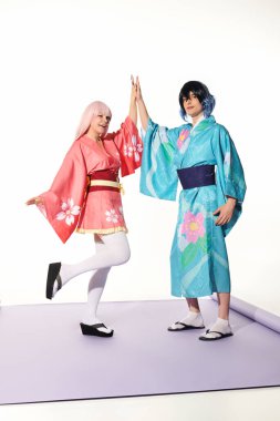 Parlak kimono ve peruklu mutlu Cosplayers mor halı ve beyaz fon üzerinde beşlik çakıyor