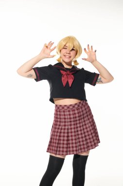 funny cosplay woman in yellow blonde wig and school uniform showing scaring gesture on white clipart