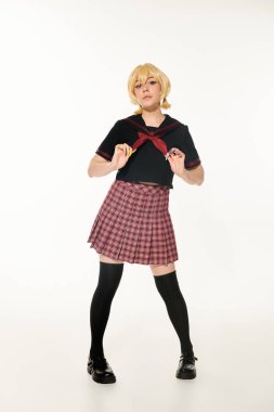 Ekose etekli, kırmızı atkıya dokunup beyaz kameraya bakan kendine güvenen anime tarzı kadın.