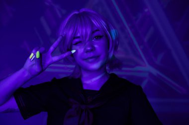 Sarışın anime kadın floresan manikürlü göz kırpan ve zafer işareti gösteren mavi neon ışıklı.