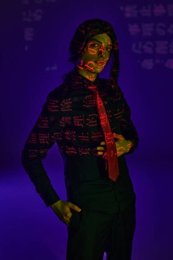 student in black wig and uniform looking at camera in neon light with hieroglyphs on blue  backdrop clipart