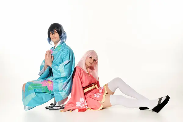 anime style man in kimono with praying hands near woman in blonde wig sitting on white, cosplayers
