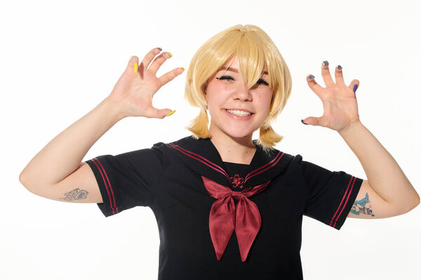 cheerful tattooed woman in school uniform showing frightening gesture on white, cosplay concept