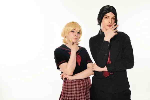 stock image serious students in dark uniform with hands near faces looking at camera on white, trendy cosplayers