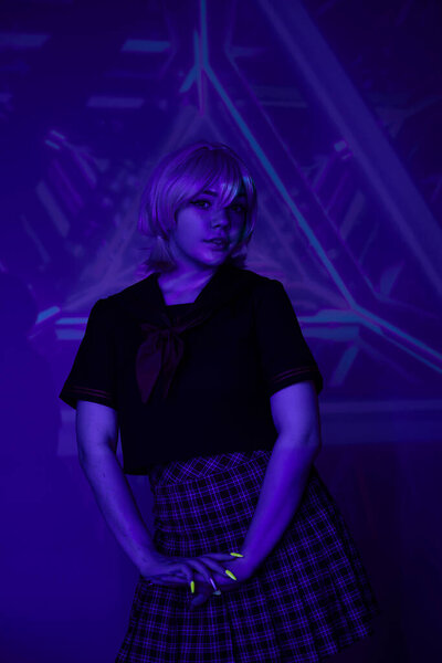 young blonde woman in school uniform in neon light on blue abstract backdrop, cosplay character