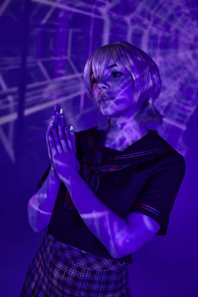blonde cosplay woman in school uniform standing with praying hands in blue abstract projection