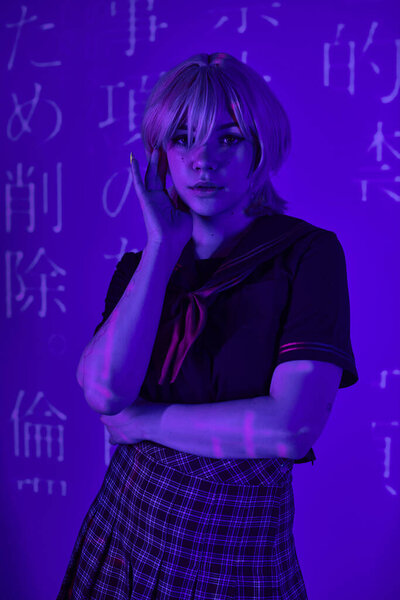 woman in blonde wig and school uniform in blue neon light with hieroglyphs projection, anime trend