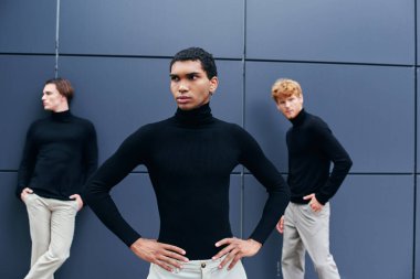 handsome african american man in black turtleneck with earring posing in front of other men clipart
