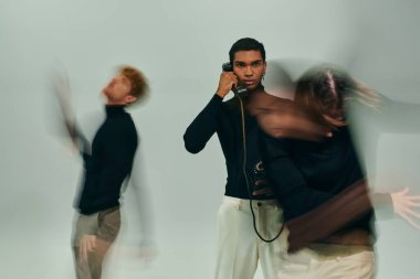 Genç Afro-Amerikan adam sabit hatlı telefonla poz veriyor diğer erkek modeller taşınıyor, uzun süre maruz kalıyor.