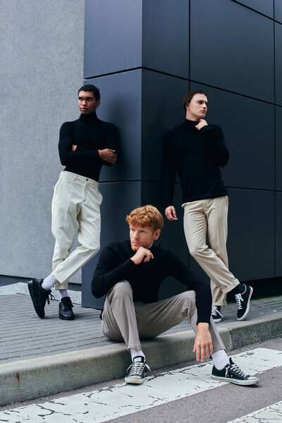 vertical shot of appealing interracial men in elegant turtlenecks posing lively on wall backdrop