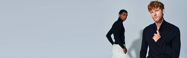 stylish red haired and african american men in black turtlenecks posing on gray backdrop, banner