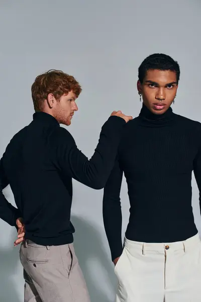 stock image vertical shot of two appealing young men in elegant attires on gray backdrop, hand on shoulder