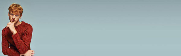 thoughtful man in red warm sweater with hand near chin looking at camera, fashion concept, banner