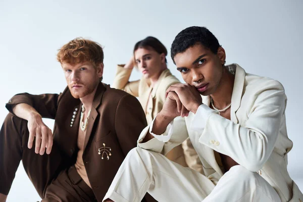 stock image focus on interracial friends near blurred young man in voguish suits sitting on floor, men power