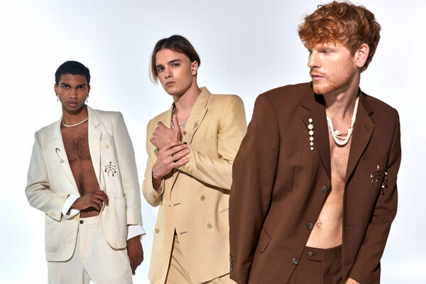 three young diverse men in elegant classy suits with accessories posing on white backdrop