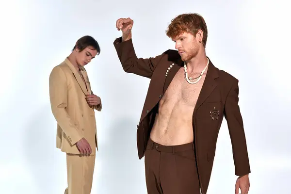 Stock image young red haired man in suit with accessories with other male model on backdrop, men power