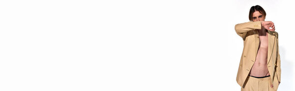 stylish young male model in unbuttoned beige suit with hand raised to face, fashion concept, banner