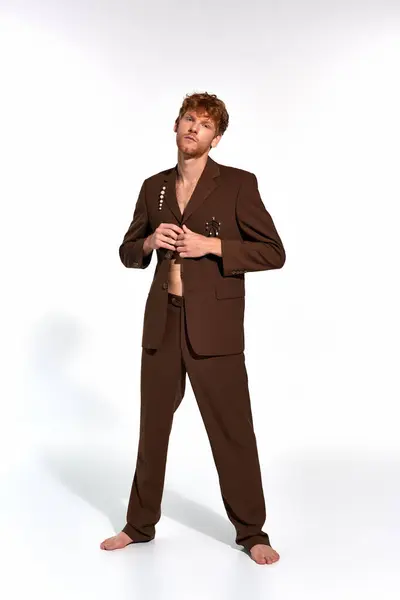 stock image vertical shot of appealing man with red hair and beard buttoning his elegant suit on white backdrop