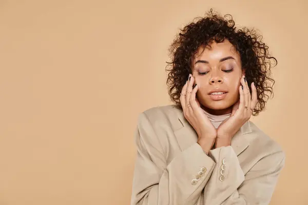 stock image autumn fashion, african american woman with closed eyes posing in blazer on beige background