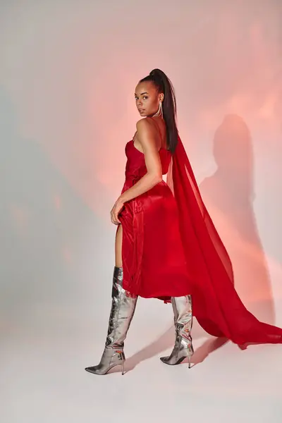 stock image charming african american woman in red dress with shawl posing in silver boots on grey with lighting