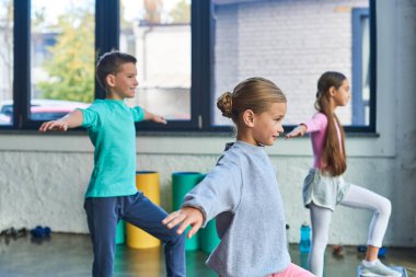 Spor giyim kuşamında üç neşeli çocuk elleriyle esneme egzersizleri yapıyor, çocuk sporu yapıyor.