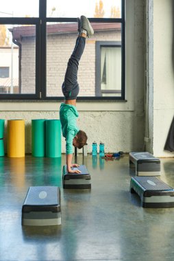 vertical shot of little boy in sportswear standing on his hands on fitness stepper in gym, sport clipart