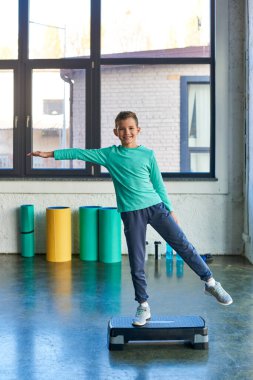 happy little boy stretching on fitness stepper and smiling cheerfully at camera, child sport
