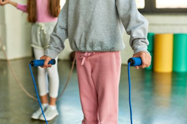 Spor giyim kuşağı giymiş, halat atlama ve çocuk sporlarıyla poz veren genç kızların kırpılmış görüntüsü.