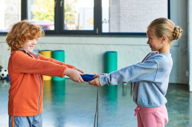 cute red haired boy and blonde girl holding jump rope and looking at each other, child sport clipart