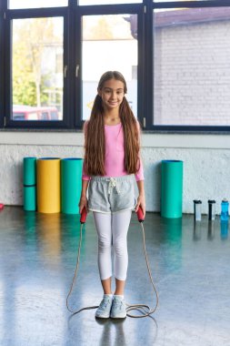 vertical shot of pretty little girl with long hair posing with jump rope in hands, child sport clipart