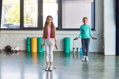 little cute boy and girl in sportswear posing with jump ropes and smiling at camera, child sport clipart