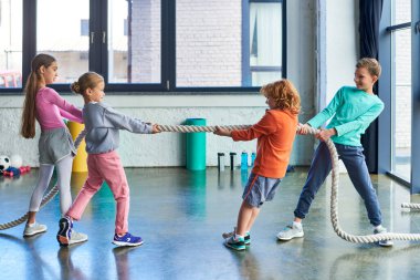 preadolescent children in sportswear playing tug of war with fitness rope in gym, child sport clipart