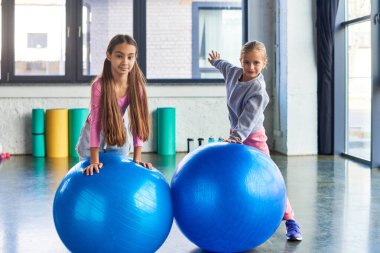 pretty preadolescent girls posing next to fitness balls and looking at camera, child sport clipart