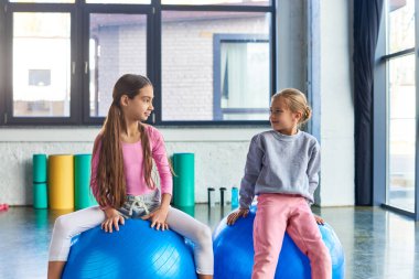 two pretty girls in sportswear exercising on fitness balls and looking at each other, child sport clipart