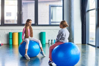 Spor giyim kuşağında güzel kızlar spor toplarının üzerinde oturup birbirlerine bakıyorlar, çocuk sporu.