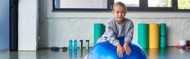 Spor kıyafetleri içinde spor salonunda uzanan ve kameraya, çocuk sporuna, pankarta gülümseyen küçük şirin bir kız.