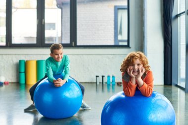 two joyful preadolescent boys exercising on fitness balls and smiling cheerfully, child sport