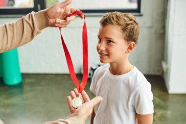 Bir adamın spor giyim ve çocuk sporlarında gençlik öncesi yakışıklı çocuğa altın madalya verdiği görüntüsü.