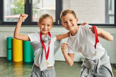 happy preadolescent boy and girl having great time wearing golden medals and smiling at camera clipart