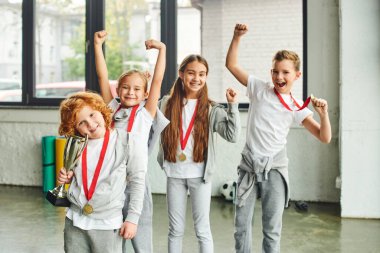 Spor kıyafetlerinde tezahürat yapan erkekler ve kızlar altın madalyalar ve çocuk sporlarıyla mutlu poz veriyorlar.