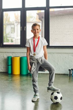 vertical shot of cute boy in sportswear with golden medal and soccer ball smiling at camera, sport clipart