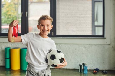 cute cheerful preadolescent boy in sportswear holding golden medal and football, child sport clipart