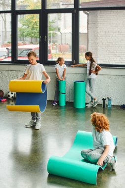 two little boys unfolding fitness mats while girls talking to each other on backdrop, child sport clipart