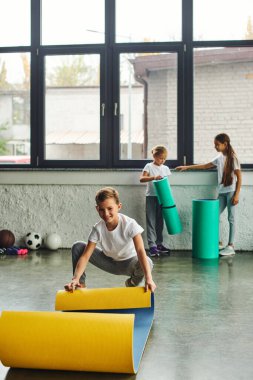 Kızlar arka planda, çocuk sporu yaparken tatlı ergenlik öncesi neşeli çocuk spor minderini açıyor.