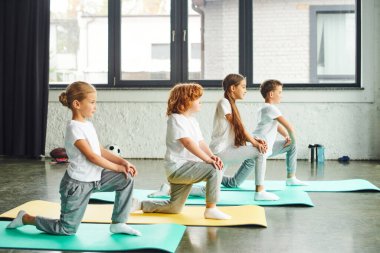 Spor kıyafetleriyle spor salonundaki küçük şirin çocuklar spor salonundaki spor paspaslarında hareketleniyorlar, çocuk sporu yapıyorlar.