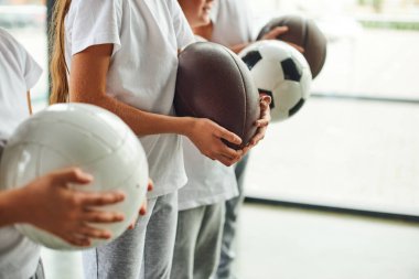 Spor kıyafetleri giymiş çocukların elinde farklı toplar, çocuk sporları...